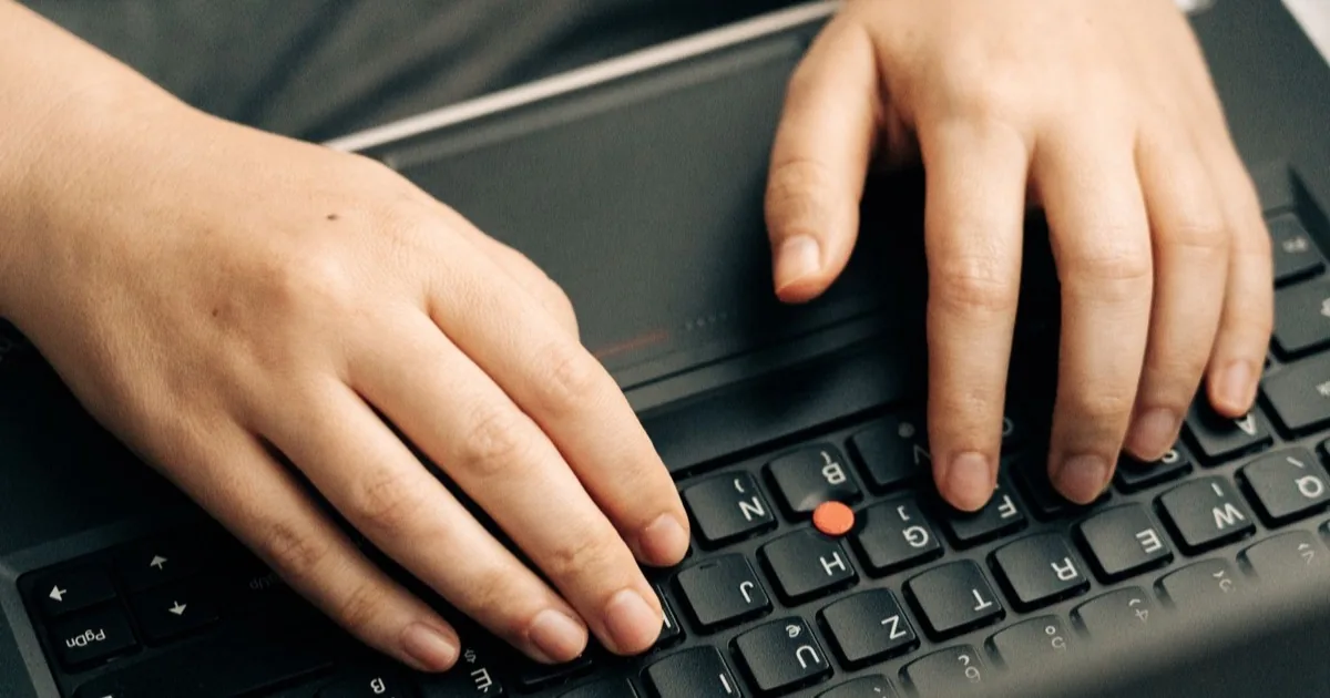 Hands resting over a laptop keyboard while someone types.