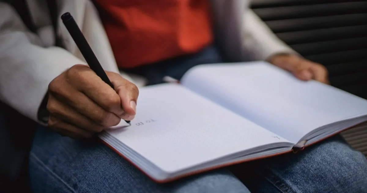 A person writing a short phrase in a notebook on their lap.