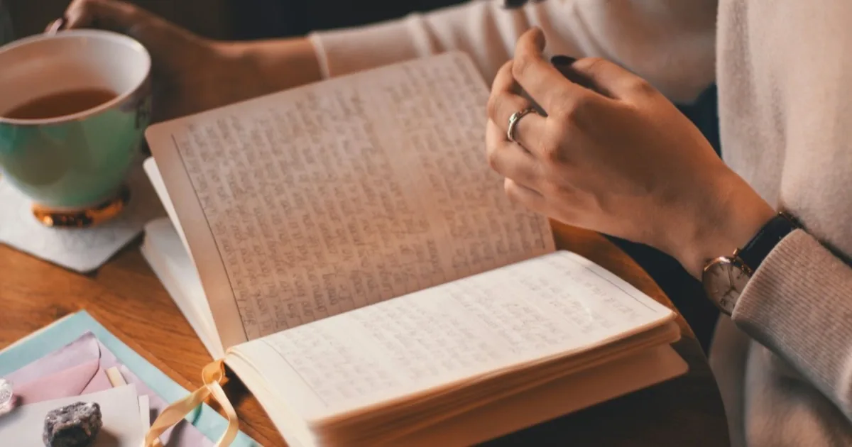 A person writing notes in a journal beside a mug.