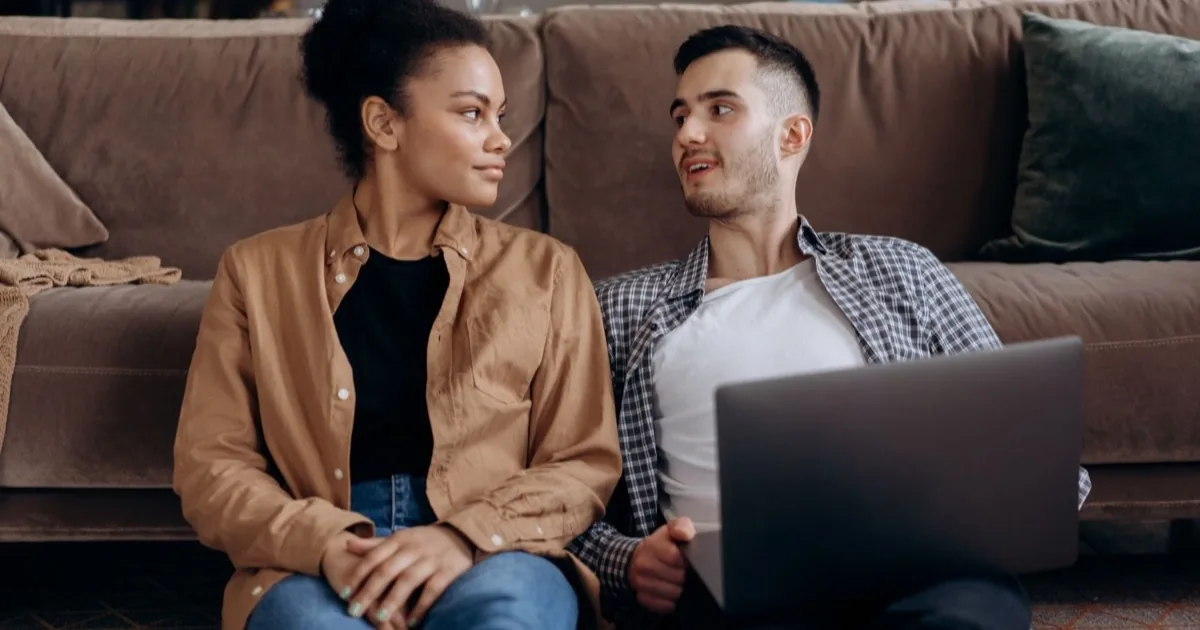 A couple talking while using a laptop together at home.