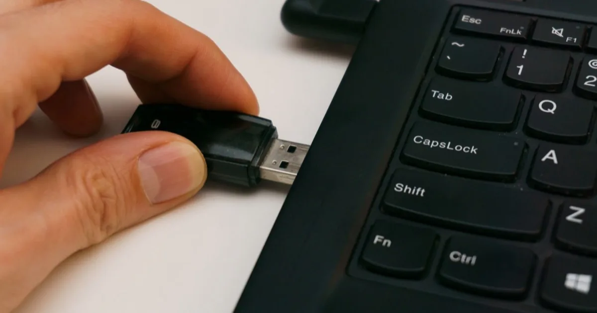 A hand inserting a USB drive into a laptop.