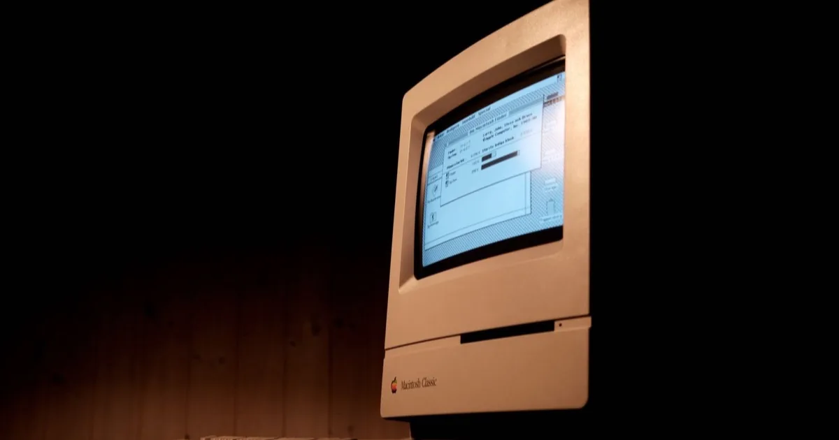 A vintage Macintosh computer glowing in a dark room.